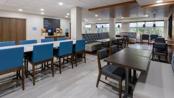 A modern dining area with multiple tables and chairs, a coffee station, and large windows providing natural light.