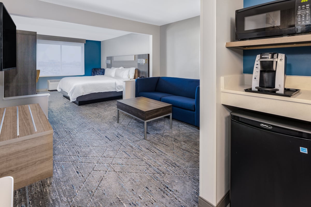 Una habitación de hotel con cama, sofá azul, cafetera, microondas y televisión.