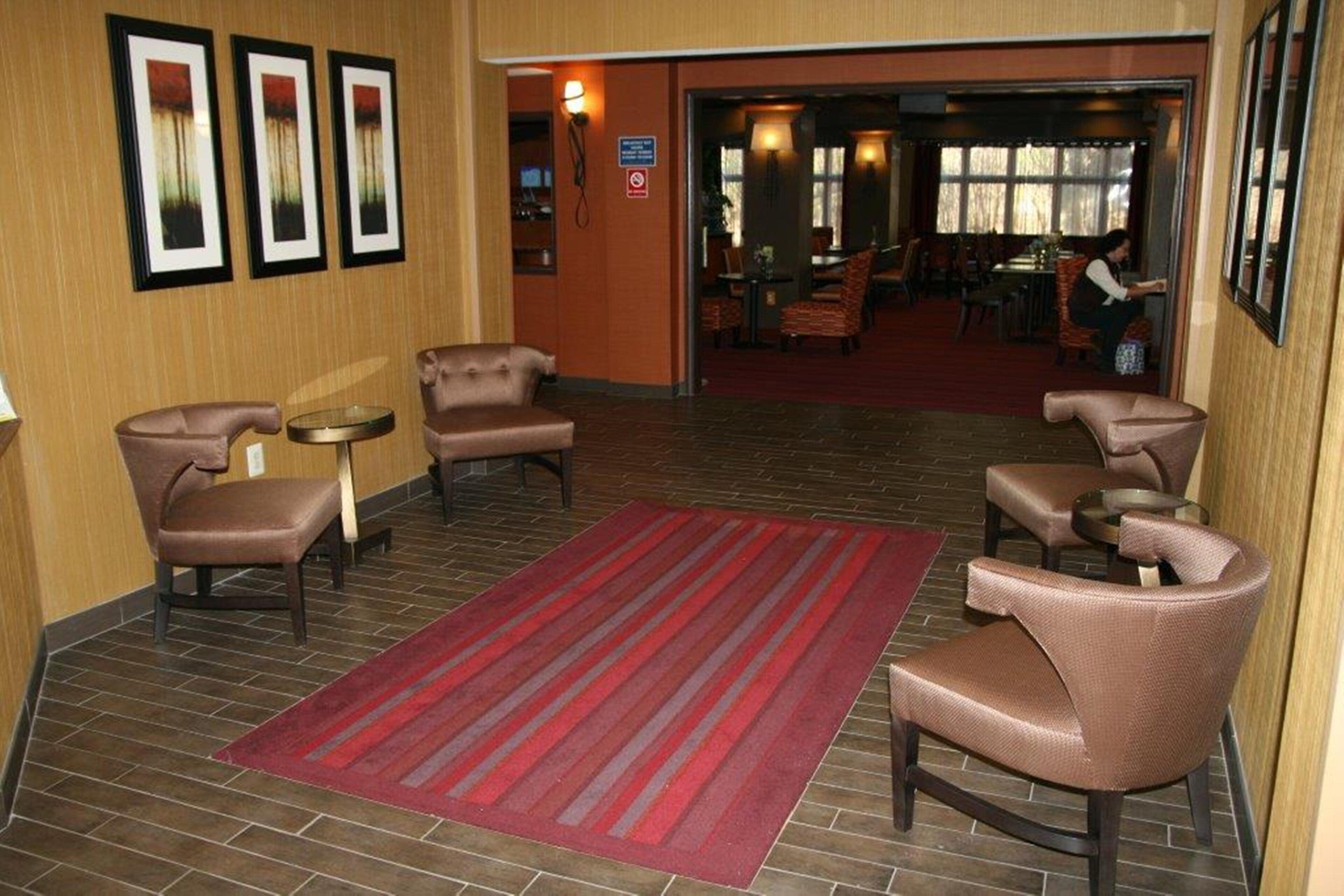 A lobby with a red carpet, leather armchairs, a small table, and framed pictures on the wall.