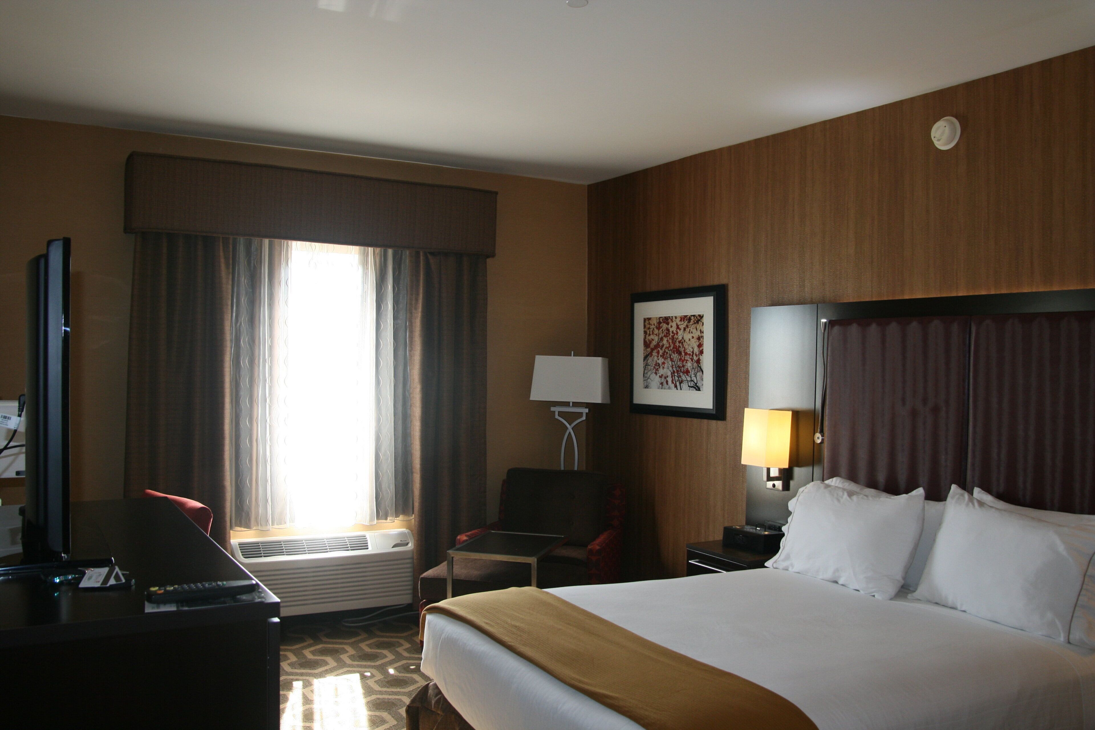Habitación de hotel con cama, escritorio, silla, lámpara y ventana con cortinas.