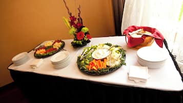 Una mesa de buffet con diversos platos, entre ellos ensaladas, verduras y un cuenco de fruta.