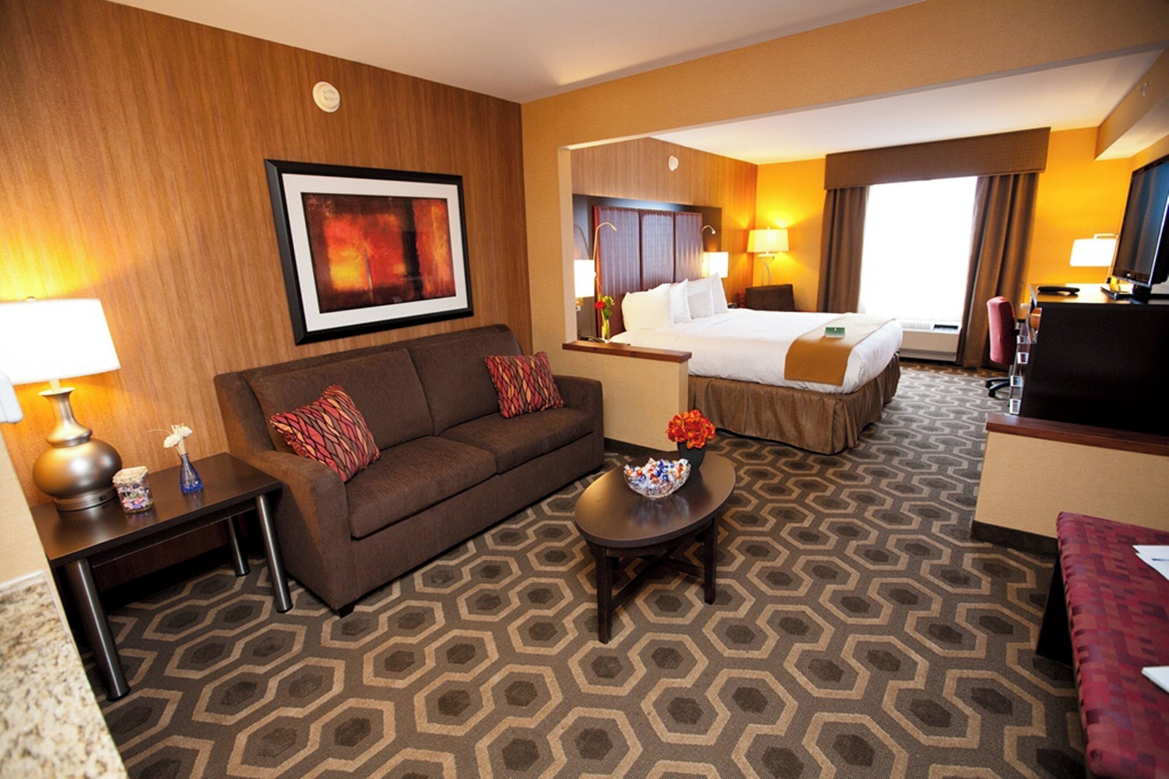 A hotel room with a sofa, a small table with a vase, a bed with a headboard, and a television.