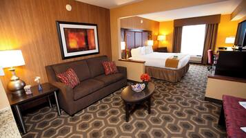 A hotel room with a sofa, a small table with a vase, a bed with a headboard, and a television.