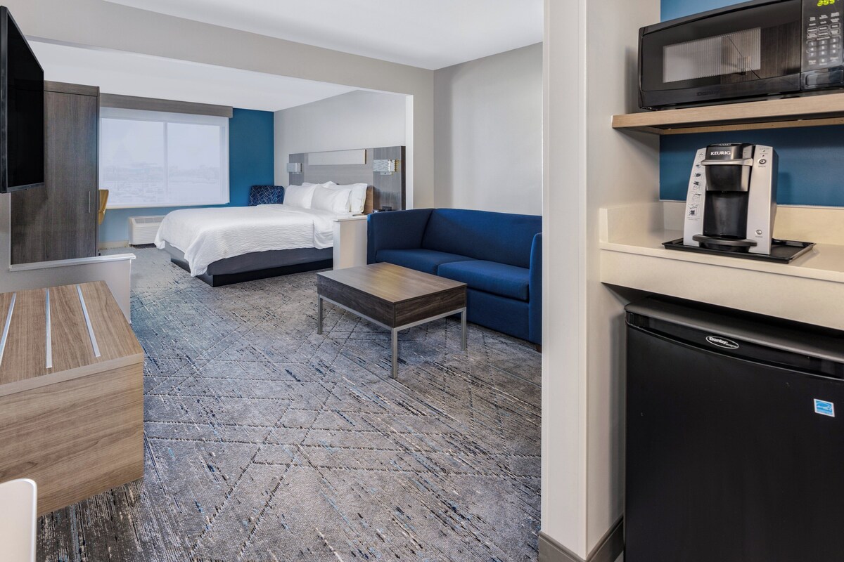 Ein Hotelzimmer mit einem Bett, einem blauen Sofa, einer Kaffeemaschine, einer Mikrowelle und einem Fernseher.