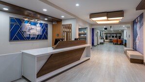 A modern reception area with a white reception desk, wooden accents, and a blue geometric wall art piece.