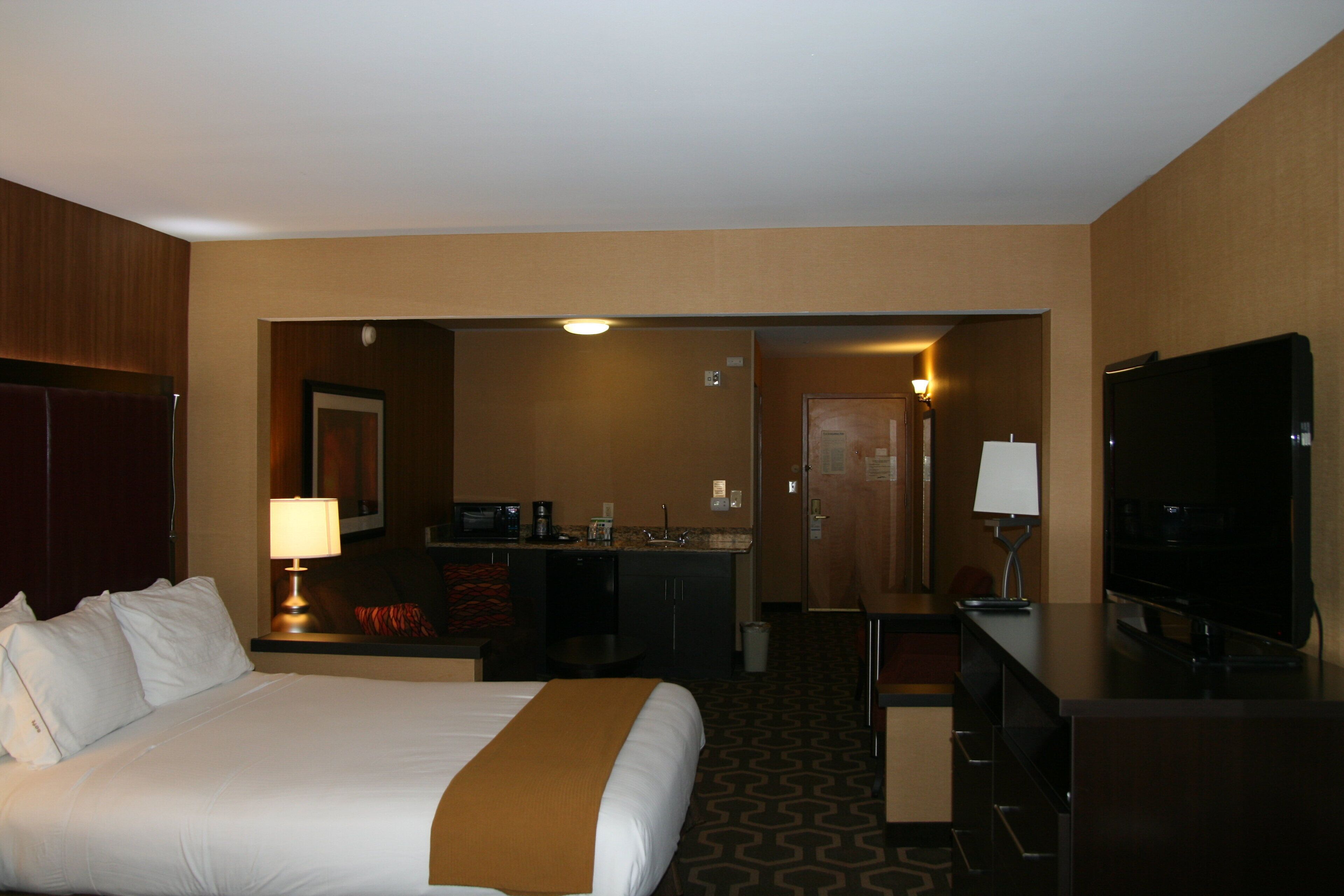 A hotel room with a bed, a desk, a television, and a kitchenette.