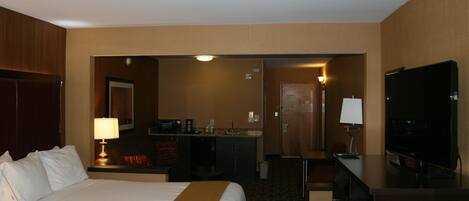A hotel room with a bed, a desk, a television, and a kitchenette.