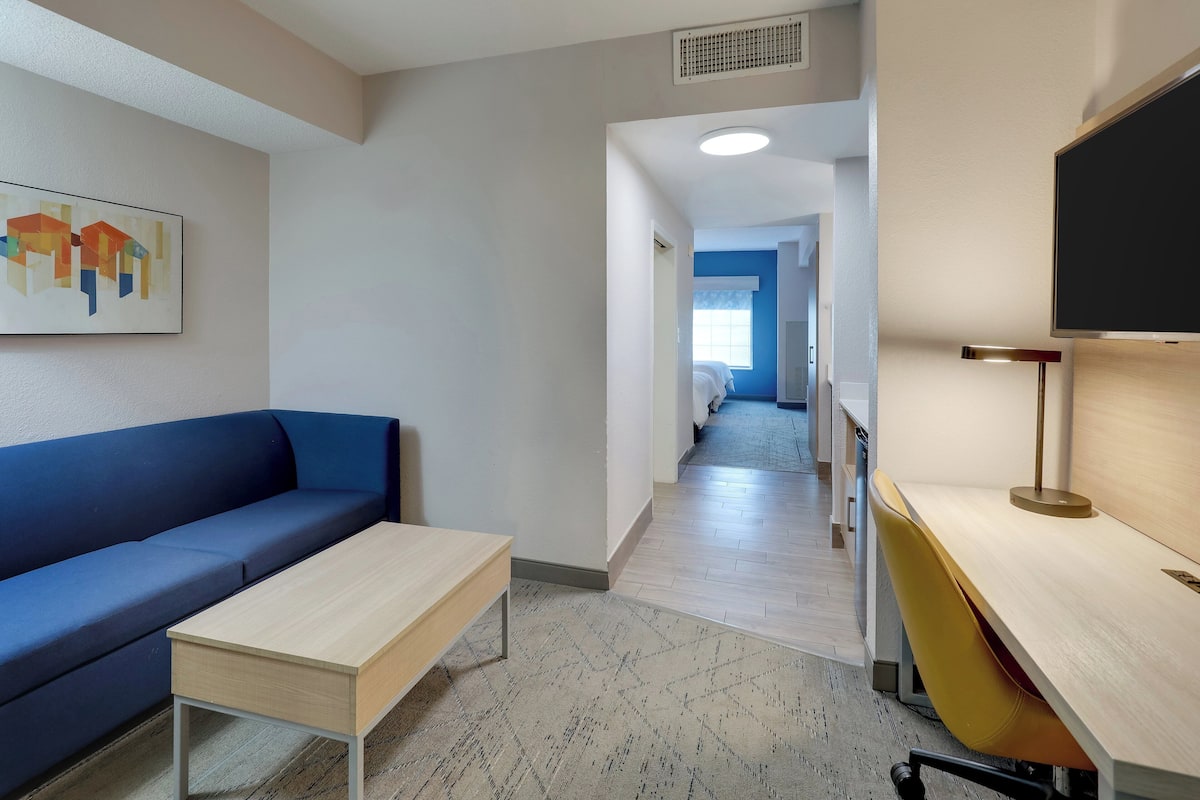 A modern hotel room with a blue sofa, a wooden desk, and a television.
