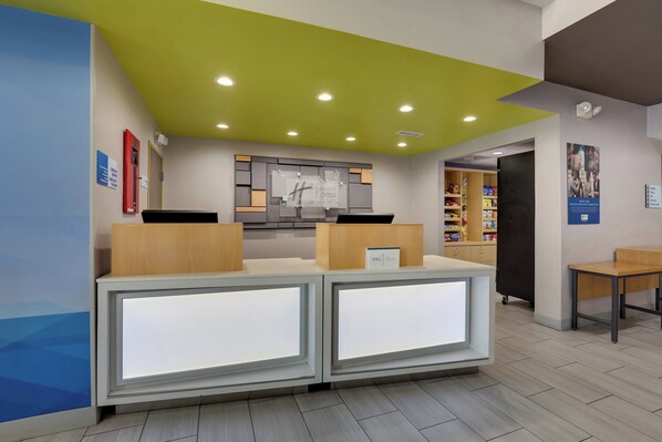 A reception area with a modern design, featuring a reception desk with illuminated panels, a green ceiling, and a wall-mounted sign.