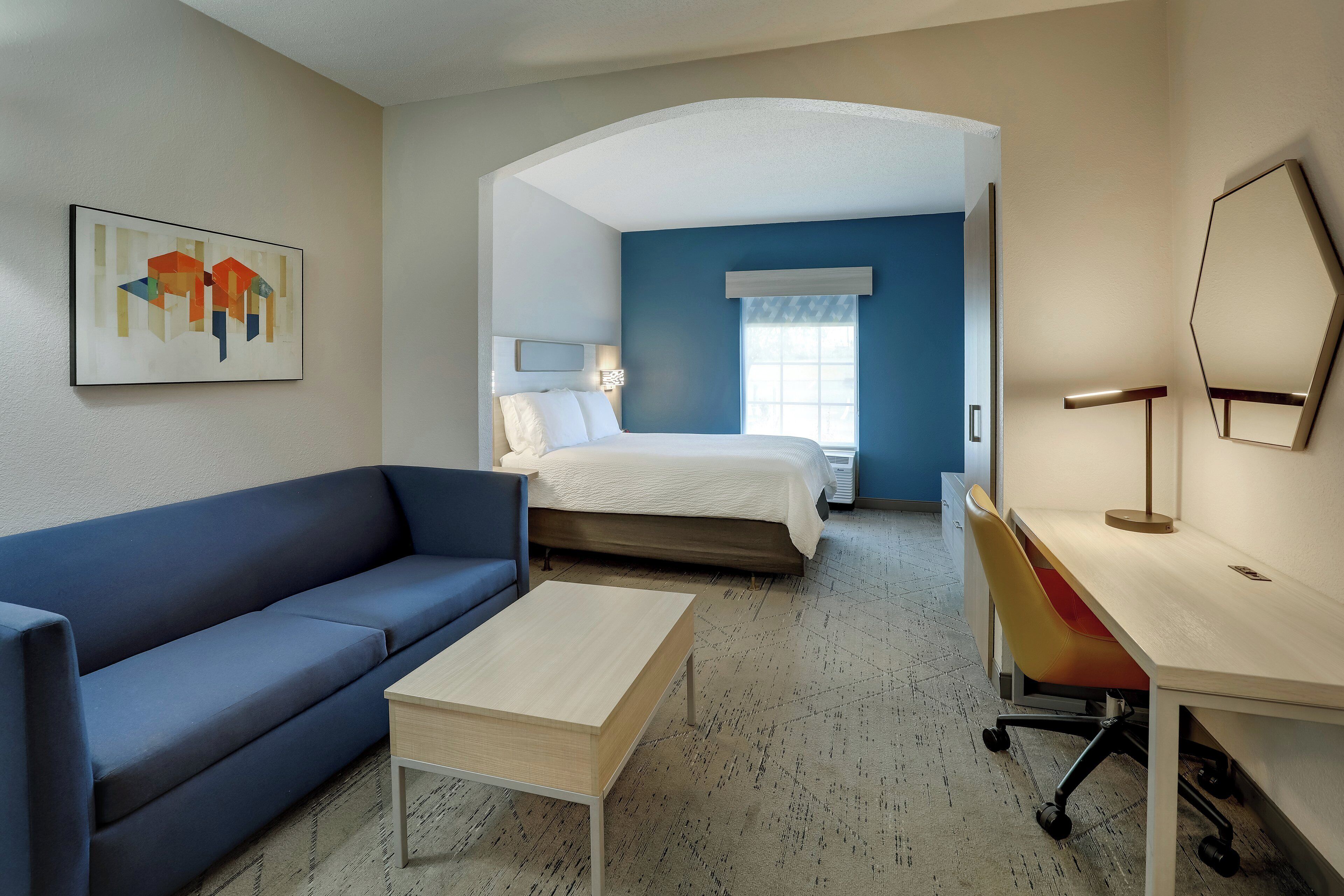 A hotel room with a bed, a blue sofa, a desk, and a painting on the wall.