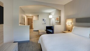 A hotel room with a large bed, a desk, a chair, a nightstand, and a wall-mounted lamp. - Holiday Inn Express & Suites Orangeburg by IHG (Orangeburg)
