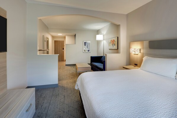 Une chambre d’hôtel avec un grand lit, un bureau, une chaise, une table de chevet et une lampe fixée au mur.