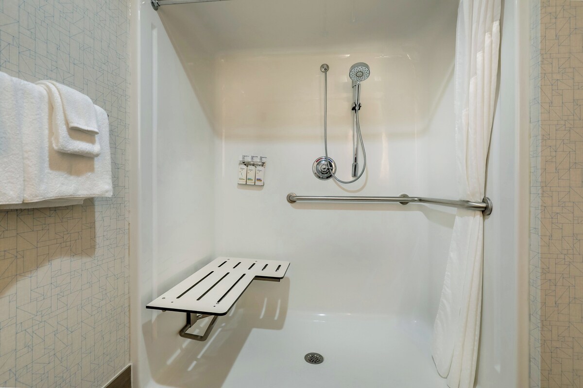 A walk-in shower with a grab bar, a towel rack, and a control panel.