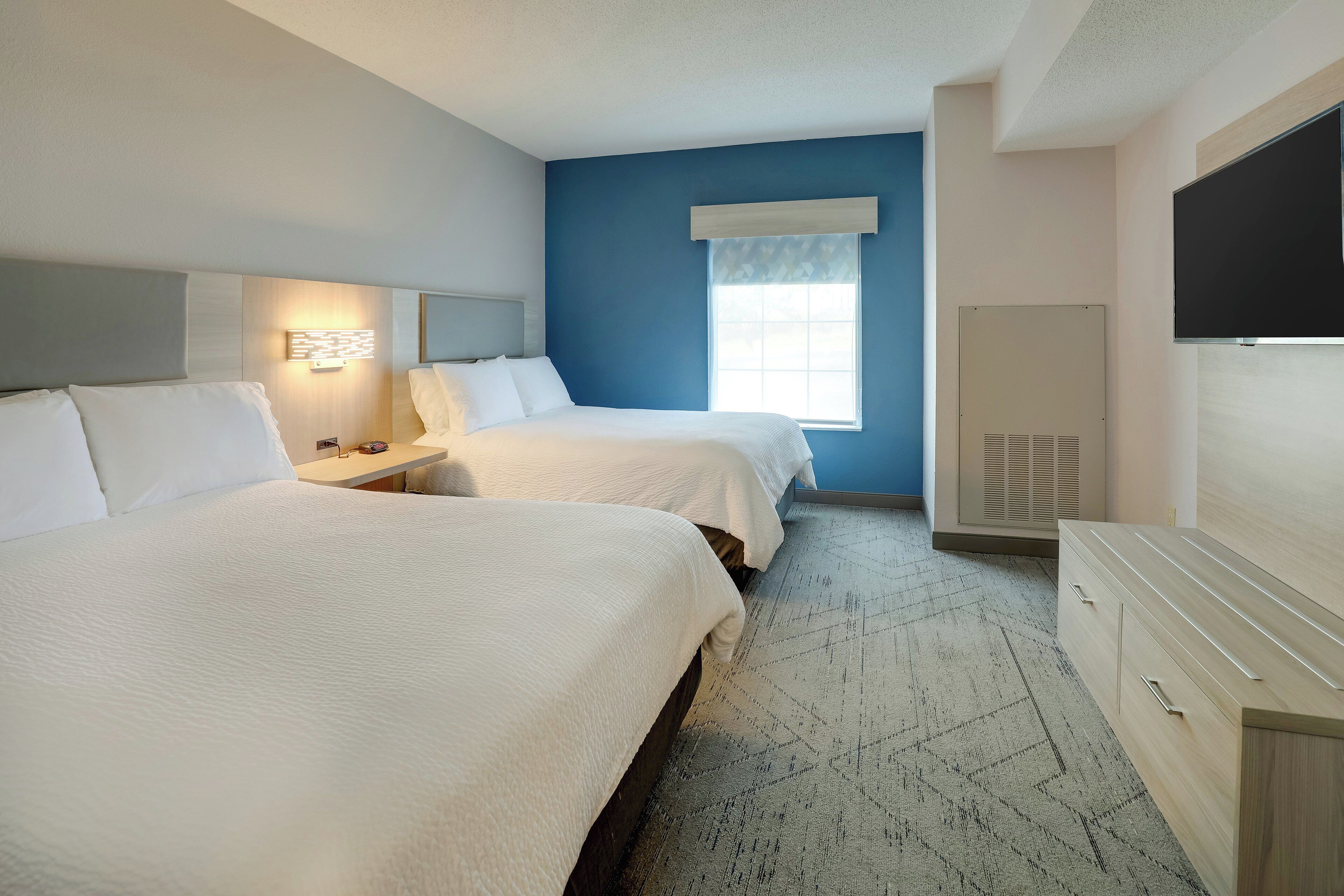 A hotel room with two beds, a large window, a flat-screen TV, and a dresser.