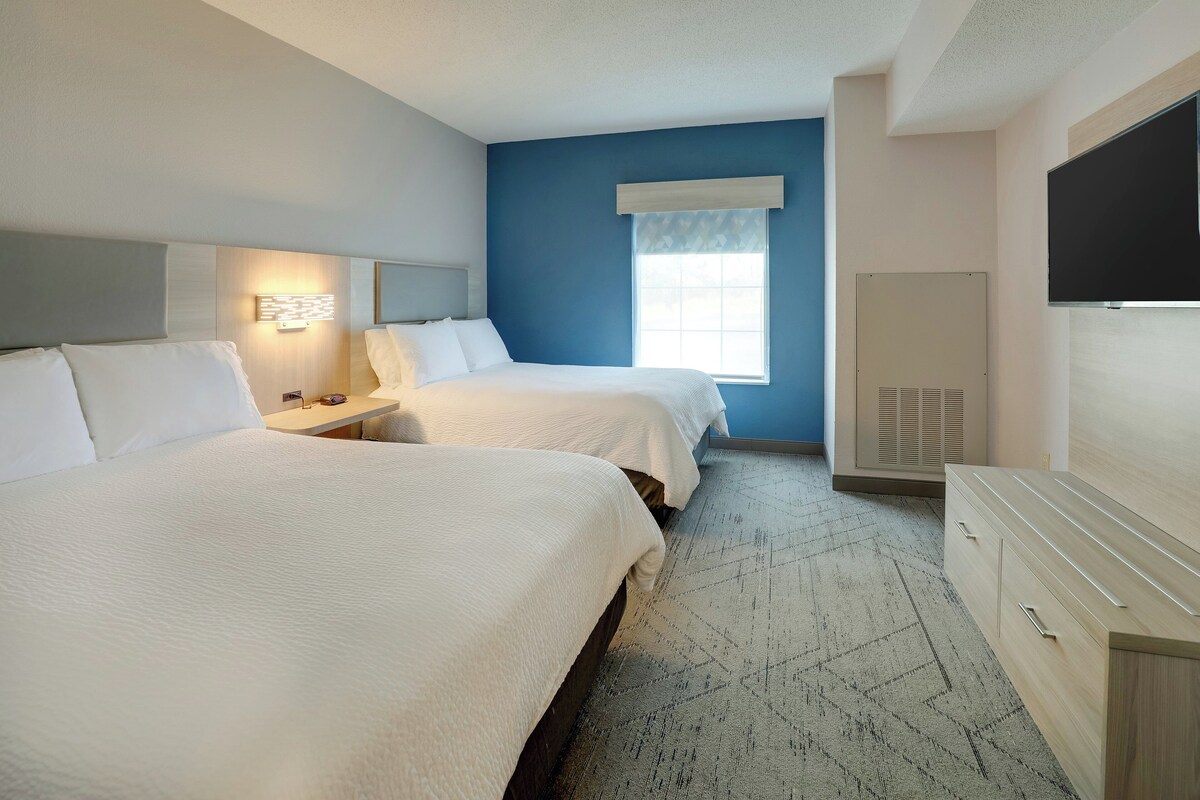 Une chambre d’hôtel avec deux lits, une grande fenêtre, un téléviseur à écran plat et une commode.