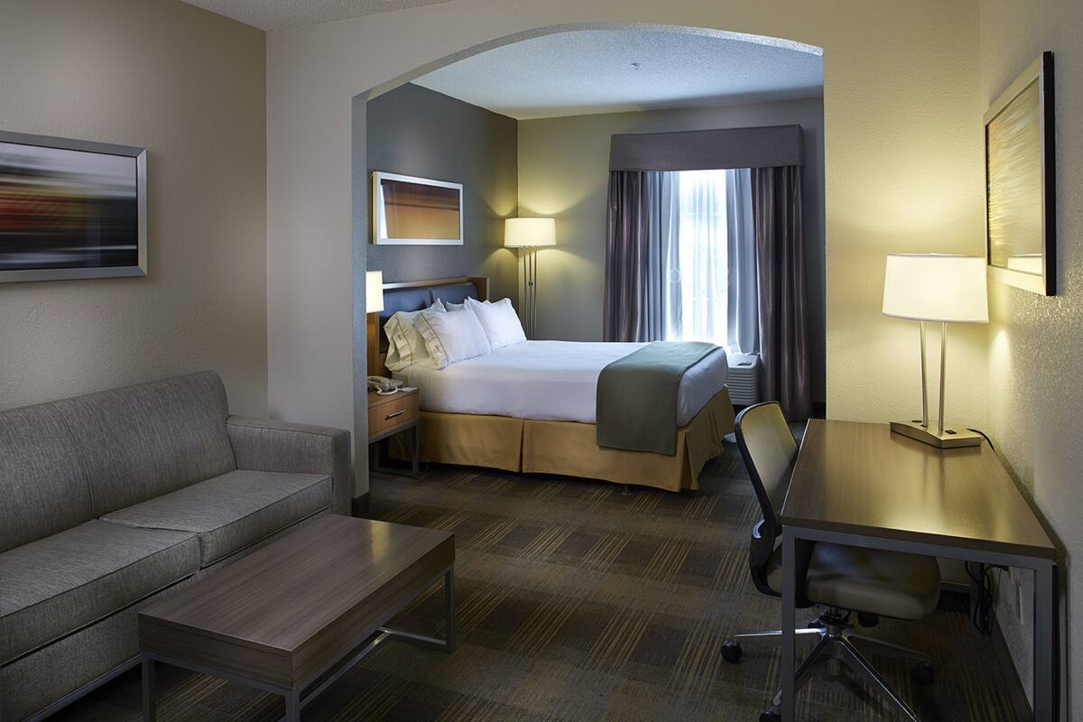 A hotel room with a bed, a desk, a chair, a sofa, and a lamp.