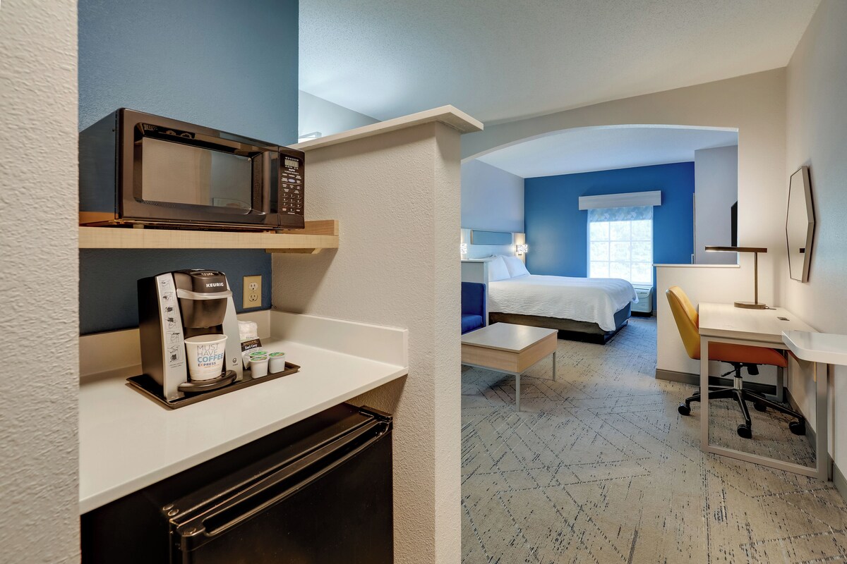 A hotel room with a kitchenette, a bed, a desk, and a chair.
