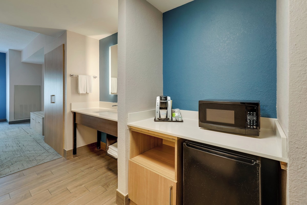A modern bathroom with a sink, mirror, towel rack, and a microwave on the countertop.