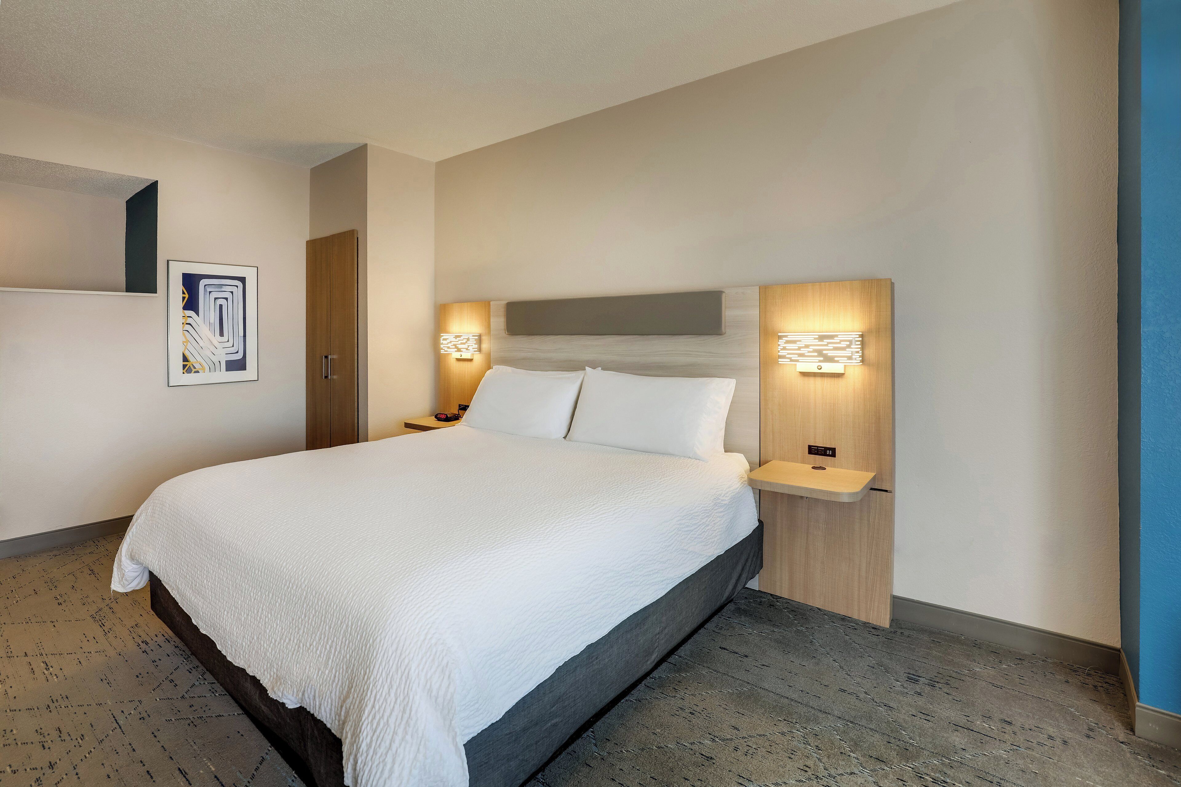 Een moderne hotelkamer met een groot bed, een houten hoofdbord en twee nachtkastjes met wandlampen.