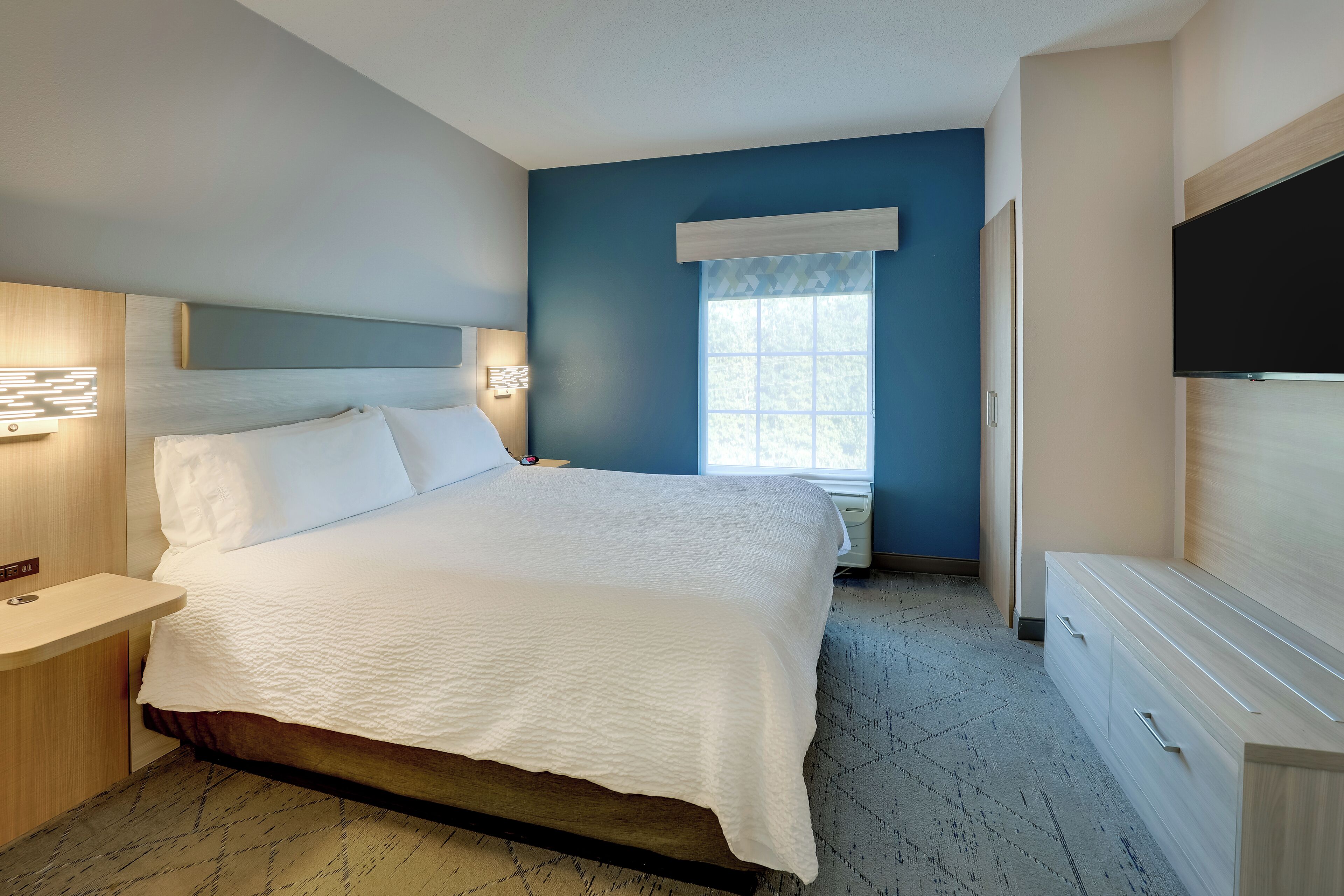 Un dormitorio con cama, mesitas de noche, televisión y ventana con vistas.