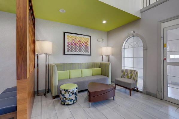 A modern hotel lobby with a green ceiling, a grey sofa, a patterned ottoman, a wooden bench, and a chair with a geometric throw. - Holiday Inn Express & Suites Orangeburg by IHG (Orangeburg)