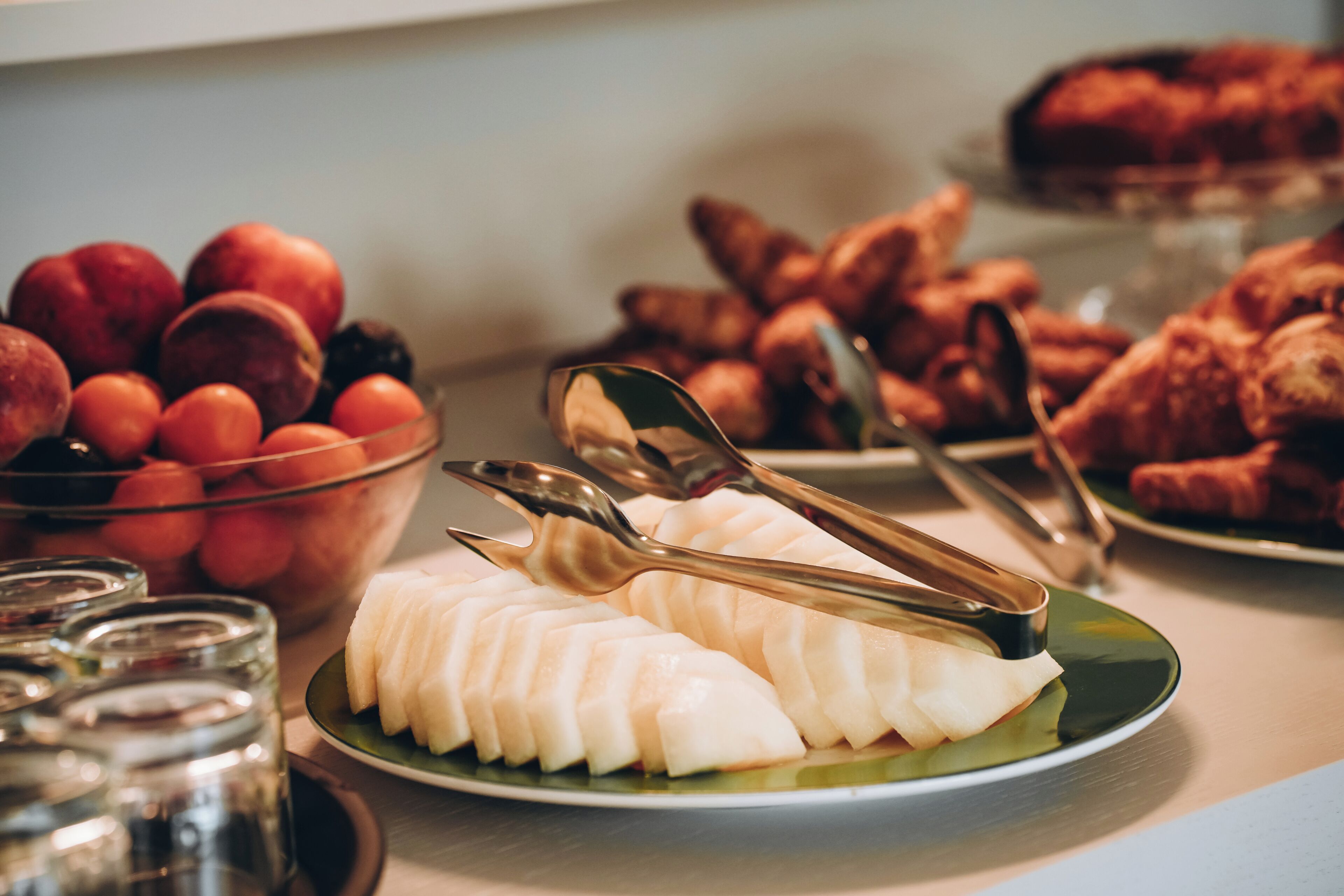 Un buffet con diversi cibi, tra cui frutta, pasticcini e un piatto di affettati bianchi.