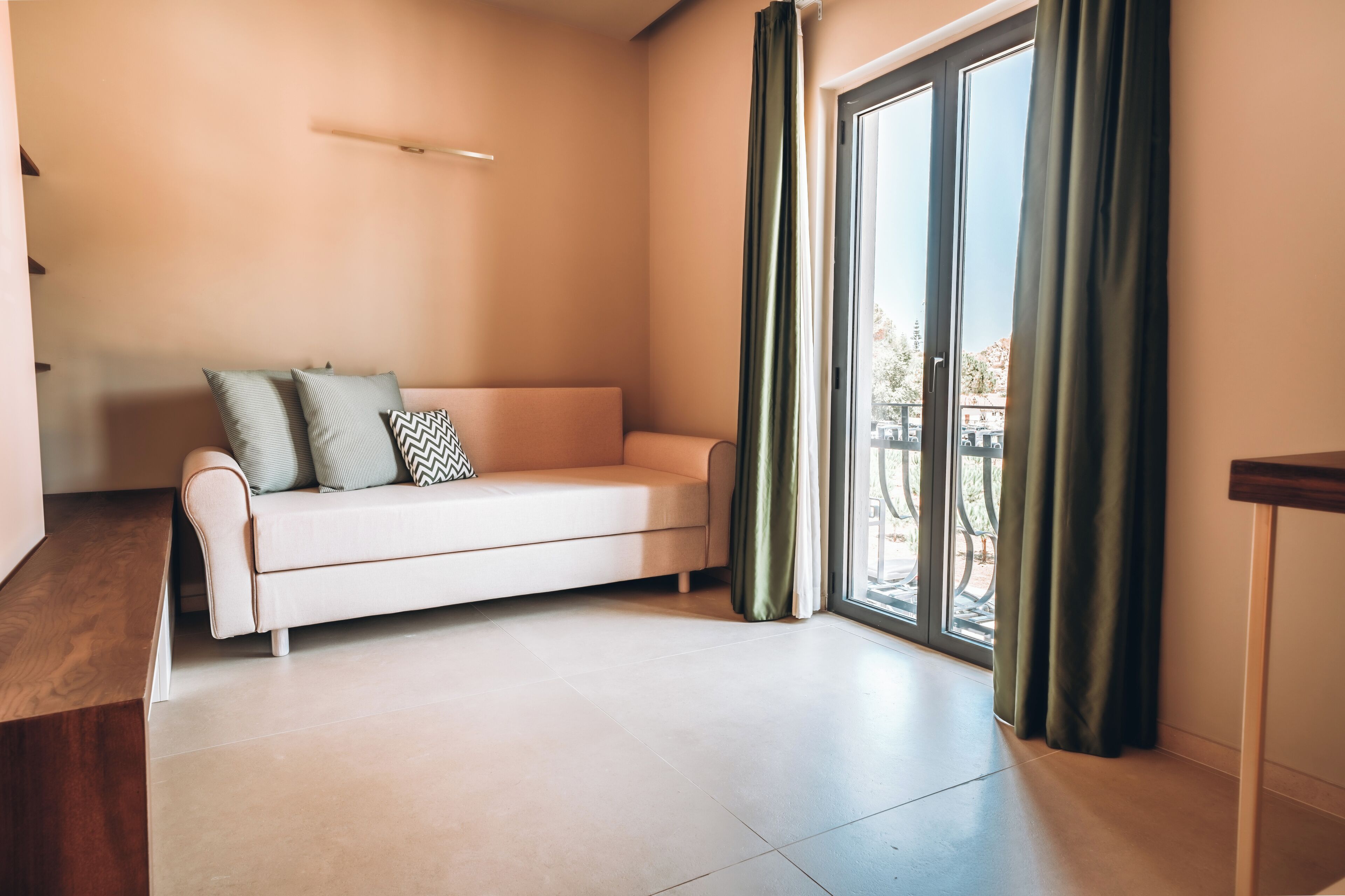 A modern living room with a sofa, a wooden bench, and a large window with curtains.