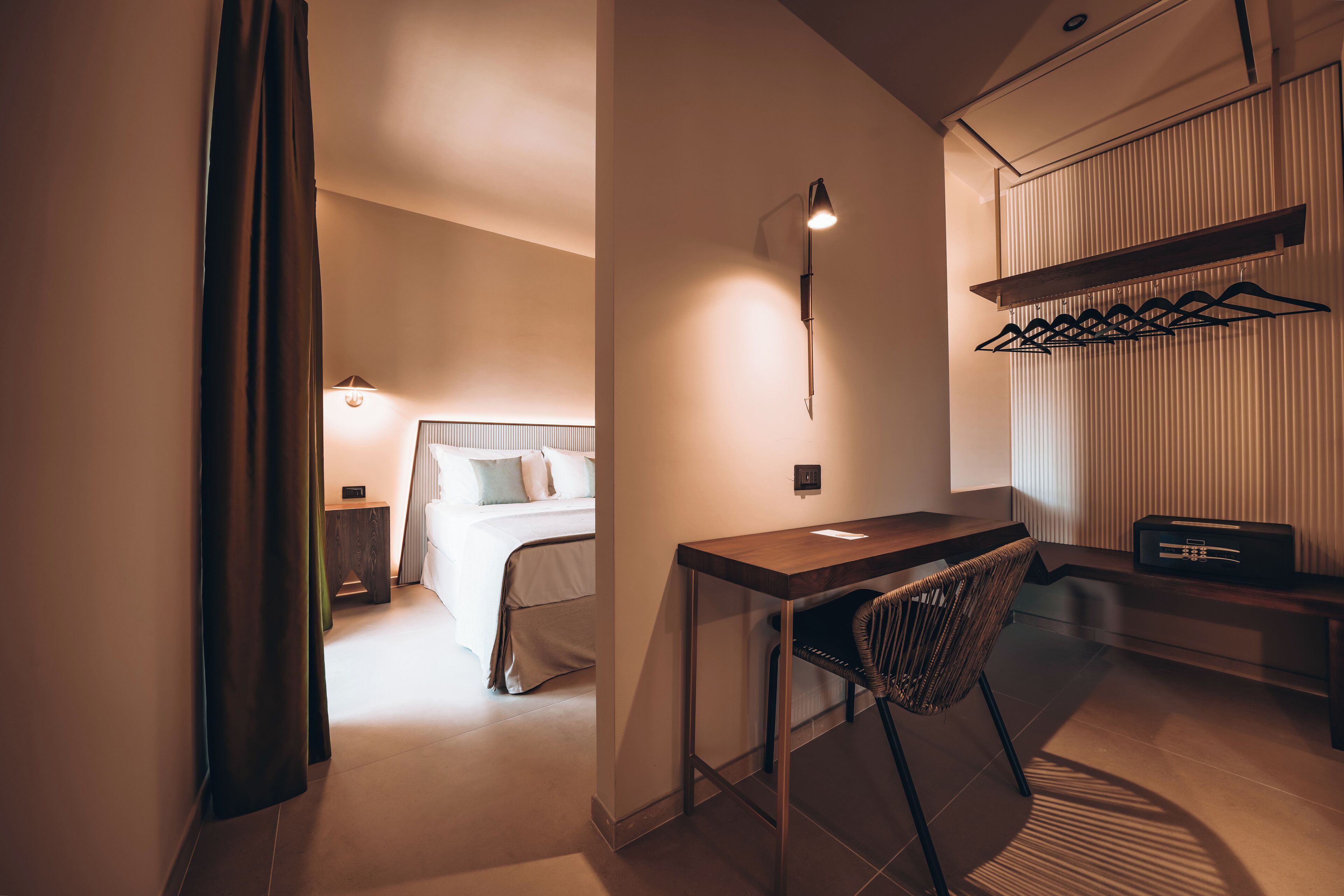 A hotel room with a bed, a desk, a chair, a coat rack, and a radio.