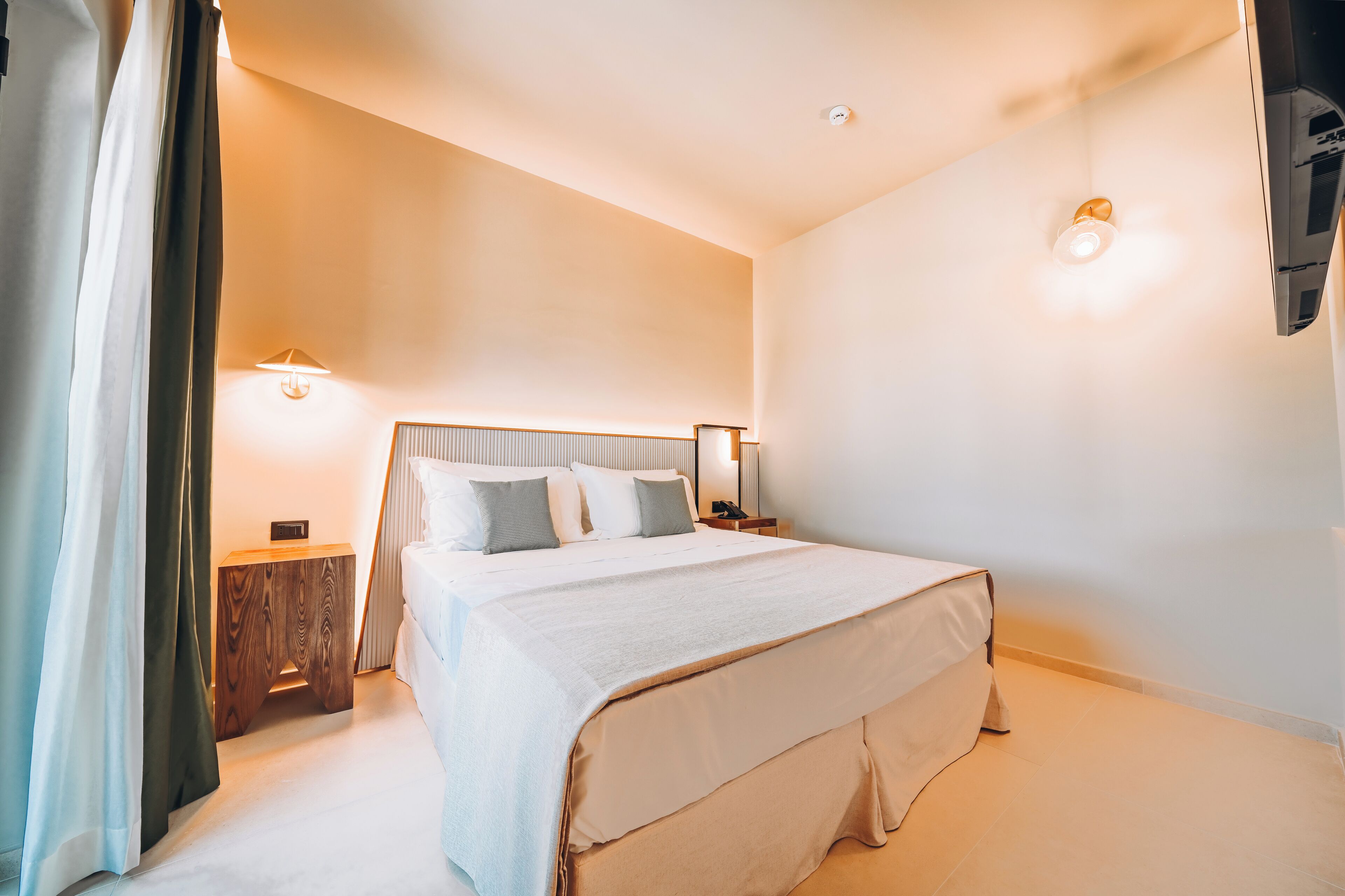 Una habitación de hotel ordenada con una cama grande, mesitas de noche y una lámpara de pared.