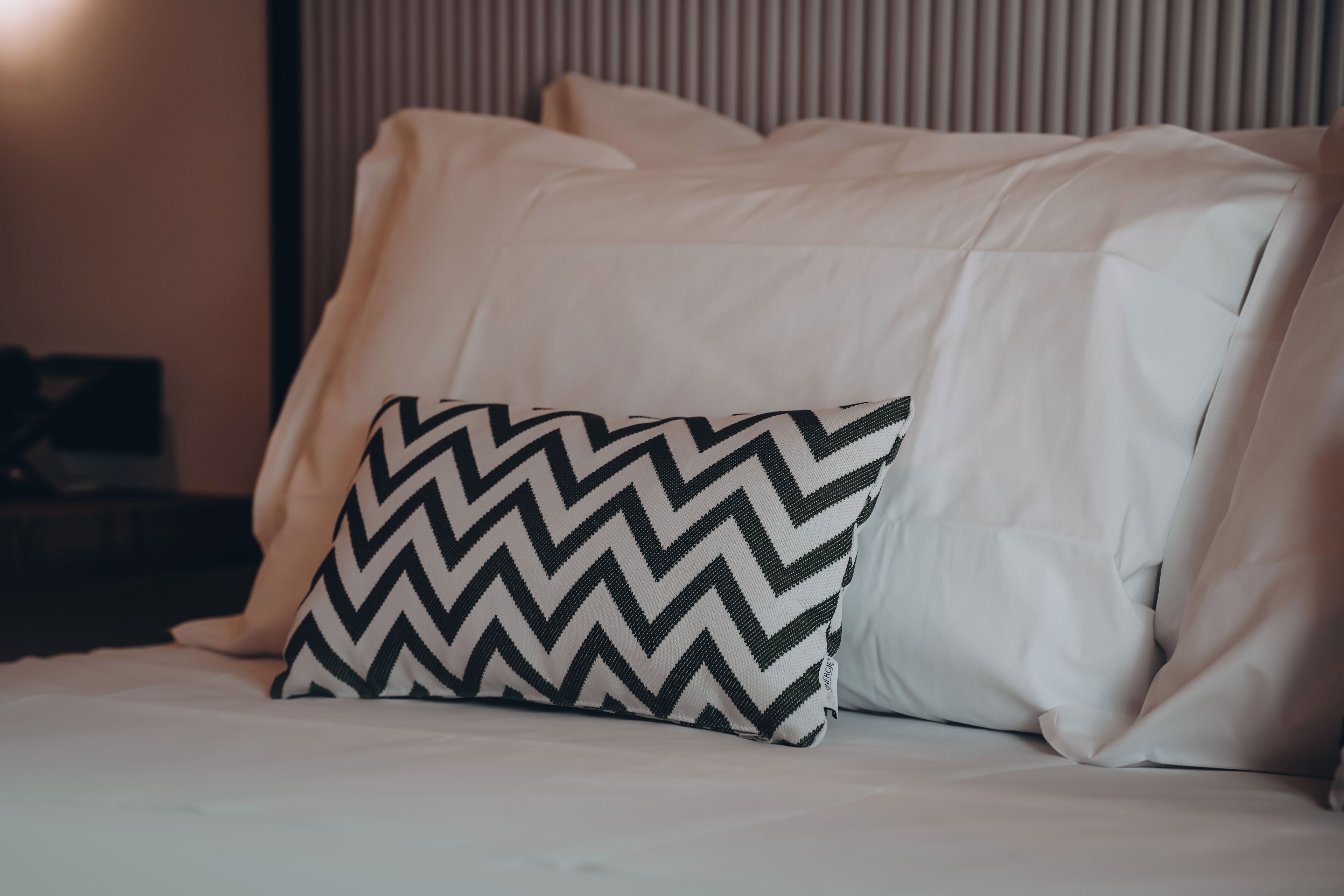 Un lit avec une literie blanche et un coussin à motifs chevrons noir et blanc.