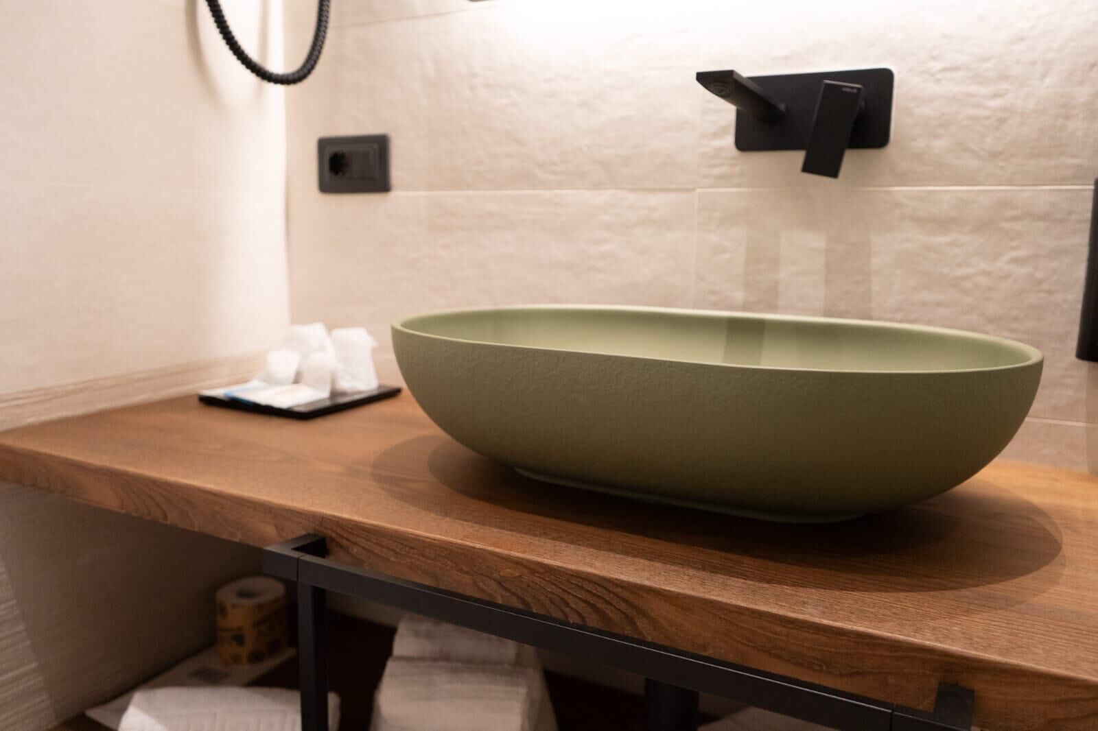 Une salle de bain avec un grand lavabo en forme de bol de couleur verte, un comptoir en bois, un distributeur de serviettes et un porte-serviettes noir.