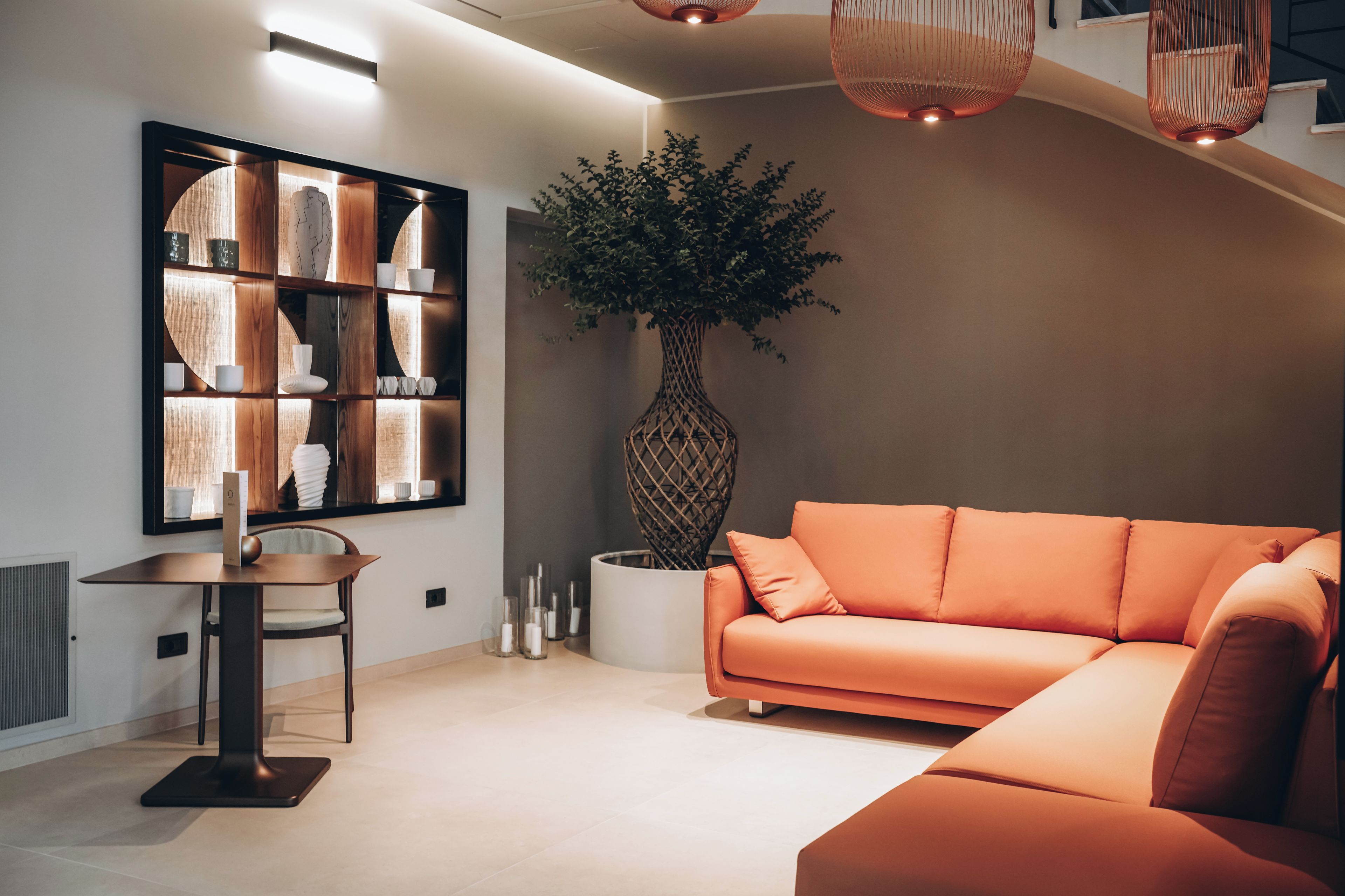 Una sala de estar moderna con un sofá seccional, una estantería de madera, una planta grande en maceta y un comedor con mesa y sillas.