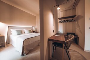 A modern hotel room with a large bed, bedside table, and a desk with a chair.
