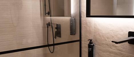 A modern bathroom with a glass-enclosed shower, a black soap dispenser, and a mirror.