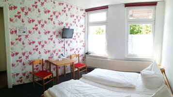 A hotel room with a bed, a desk with a chair, a television, and a window with a view of greenery.