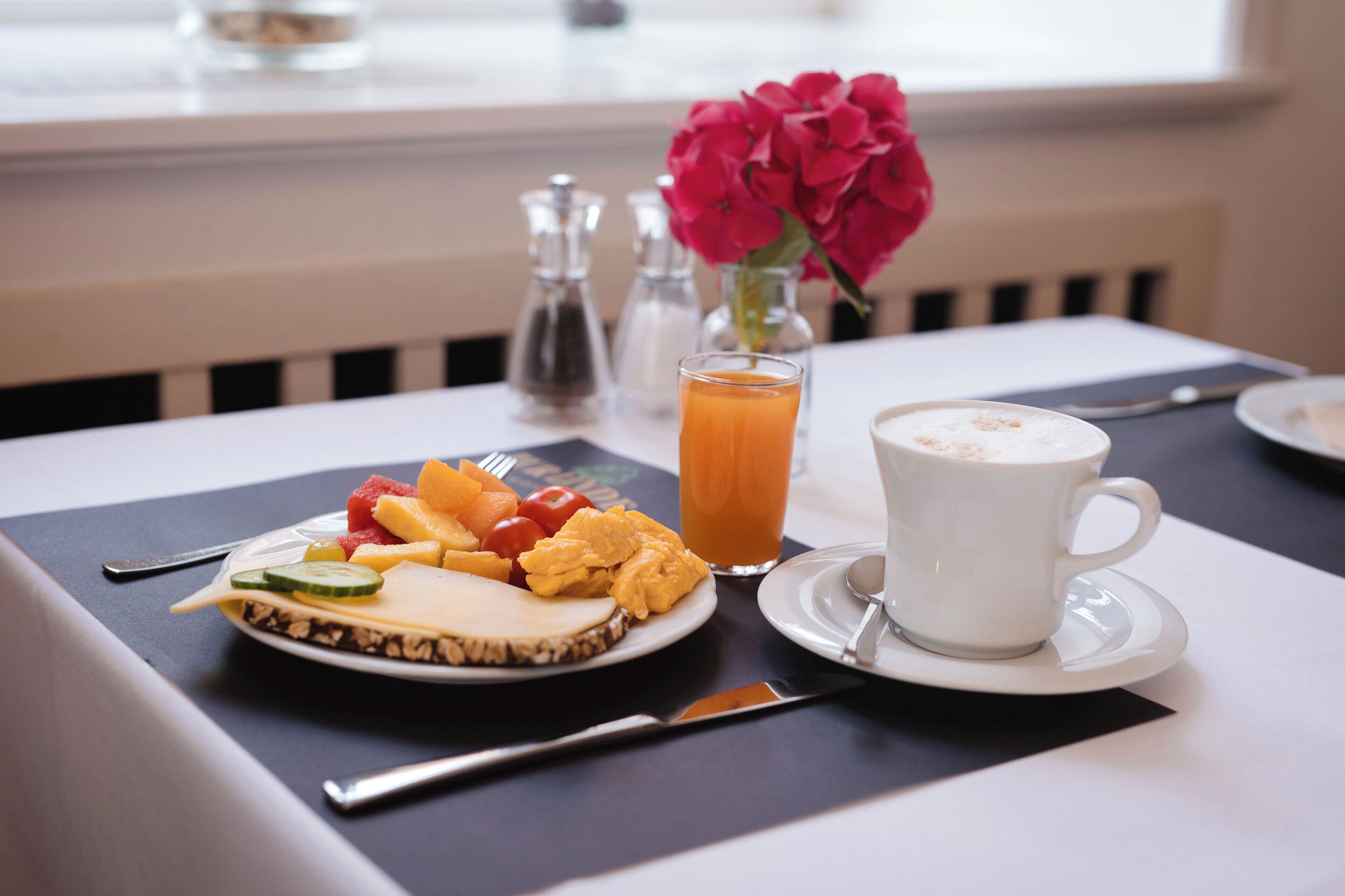 A breakfast setting with a plate of food, a glass of orange juice, and a cup of coffee on a table.