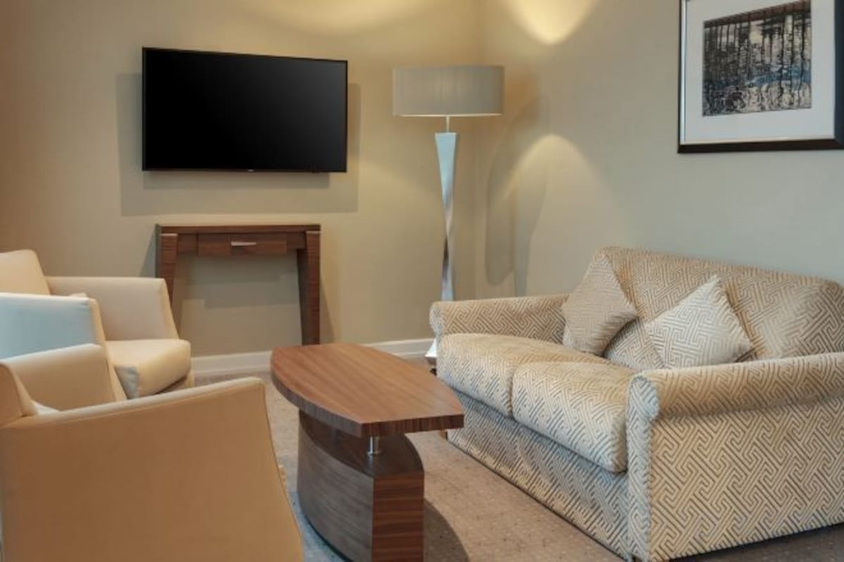 A living room with a sofa, armchair, coffee table, flat-screen TV, floor lamp, and a fireplace.