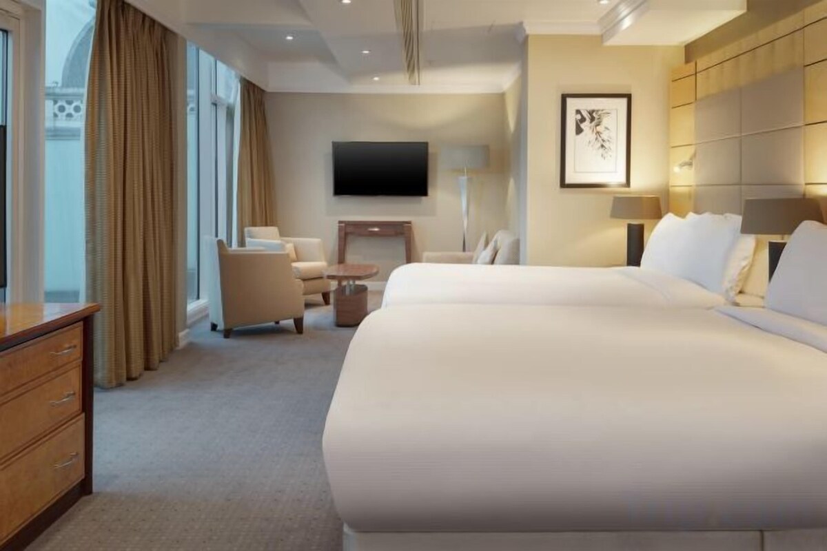 A hotel room with a large bed, a desk, a chair, a TV, and a window with curtains.