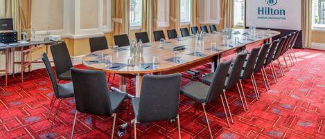 A conference room with a long table, chairs, and a projector screen displaying the Hilton logo.