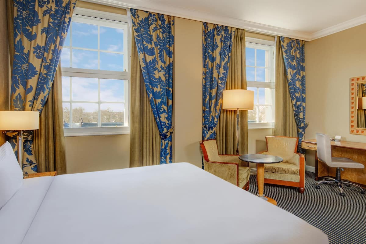 A hotel room with a large bed, two chairs, a desk, and a lamp.