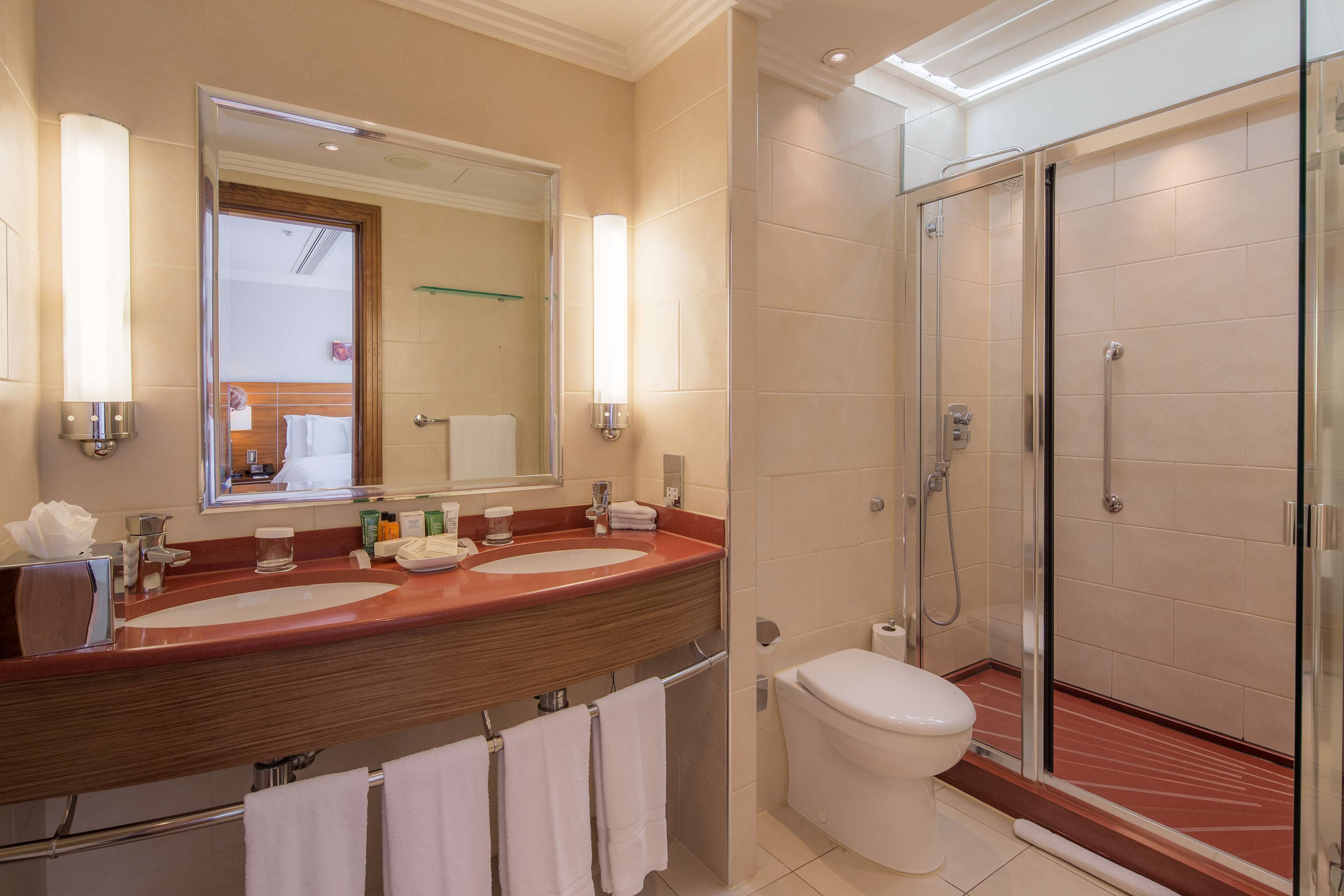 A modern bathroom with a large mirror, dual sinks, a toilet, and a glass-enclosed shower.