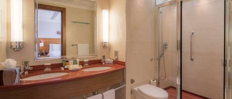 A modern bathroom with a large mirror, dual sinks, a toilet, and a glass-enclosed shower.