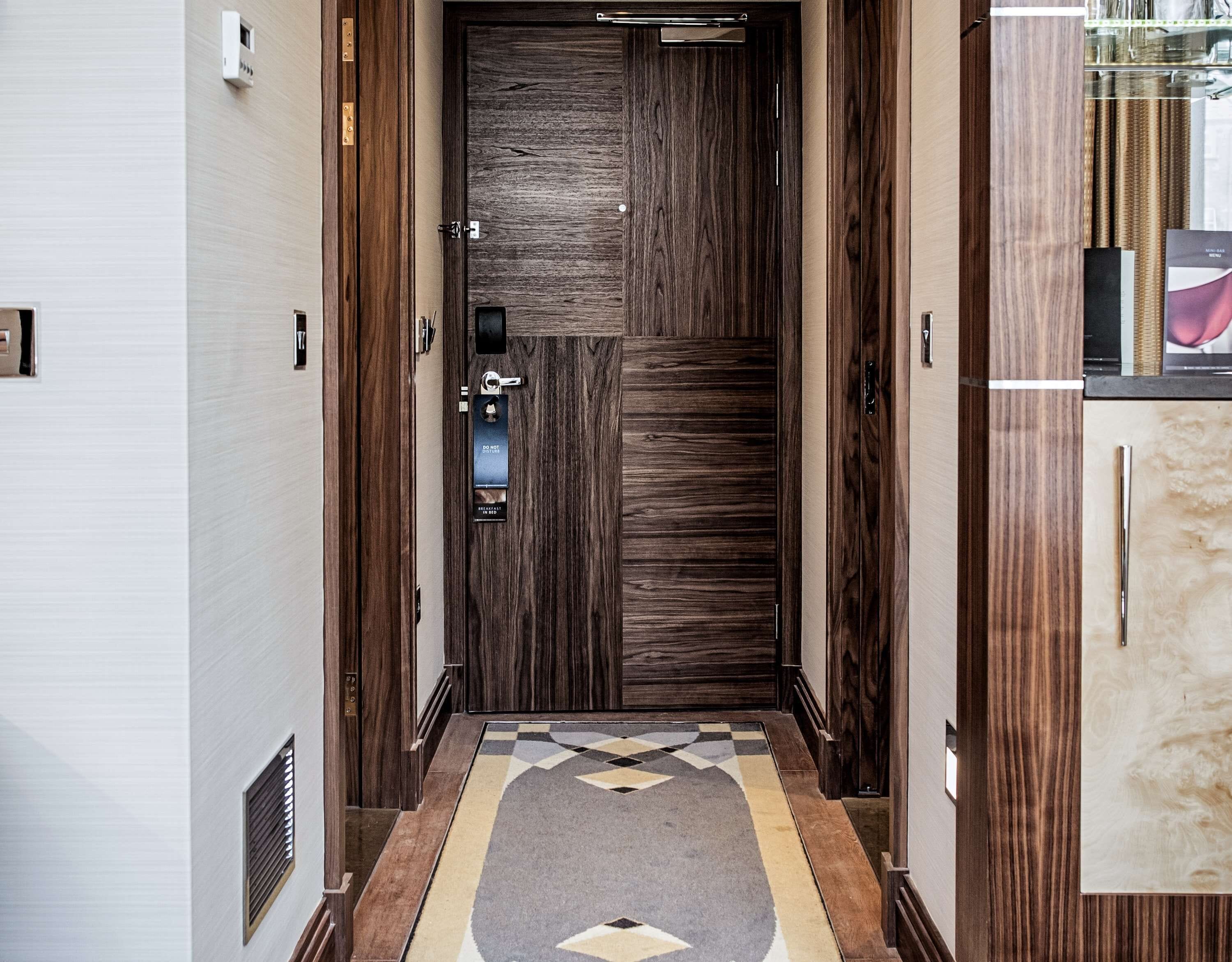 A hallway with a wooden door, a patterned rug, and a cabinet with a glass door.