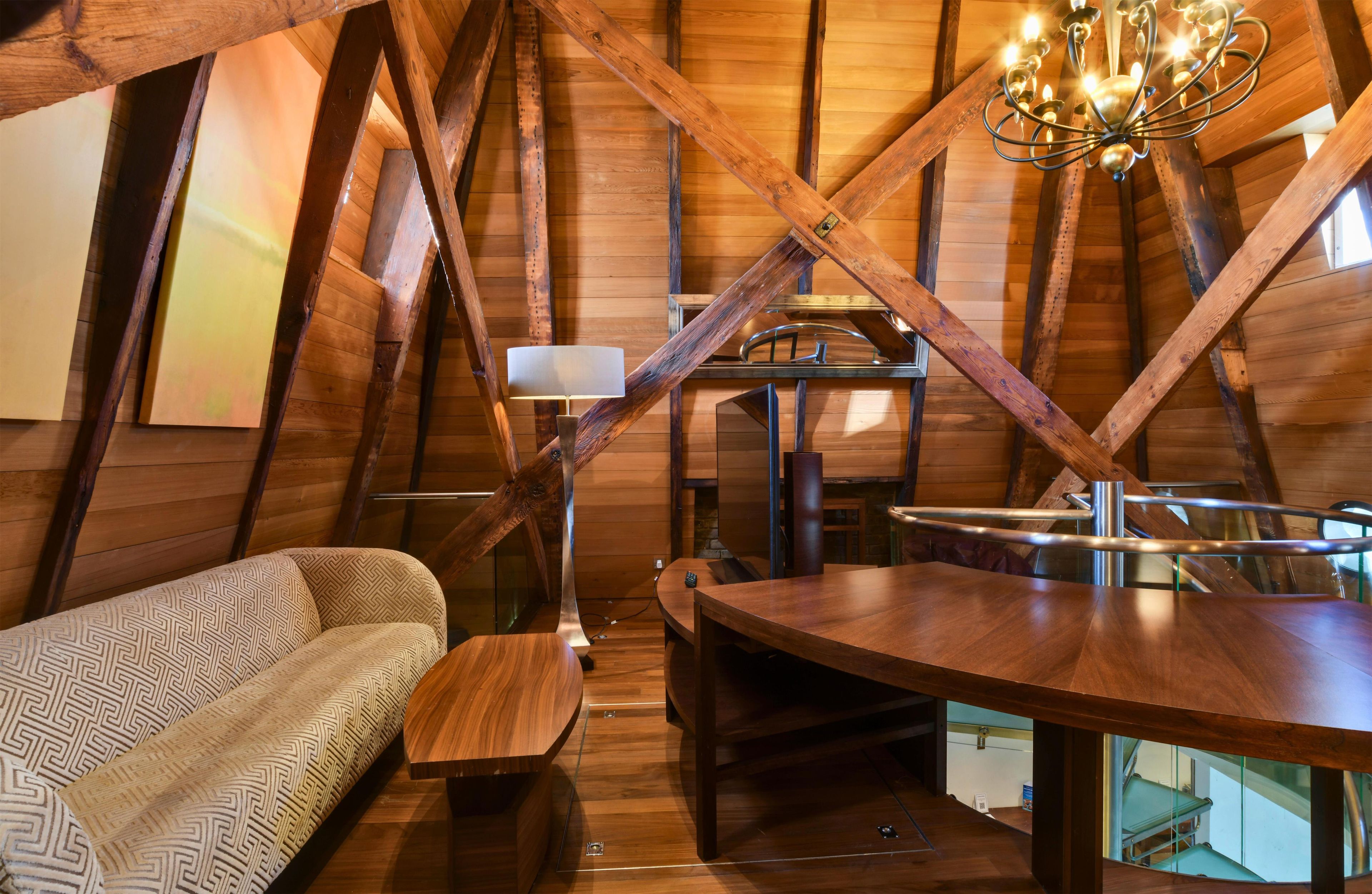 A high-ceilinged wooden room with a bed, a dining table, and a chandelier.