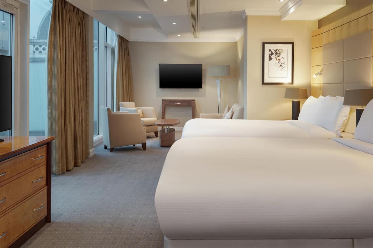 A hotel room with a large bed, a desk, a chair, a TV, and a lamp.