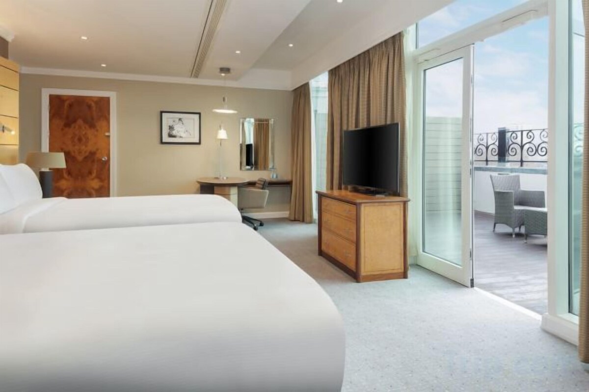 A hotel room with a large bed, a desk with a chair, a television, and a sliding glass door leading to an outdoor balcony.