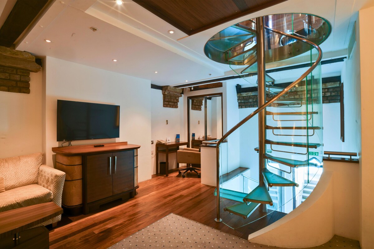 A modern interior with a spiral staircase, wooden flooring, a television, and a sofa.