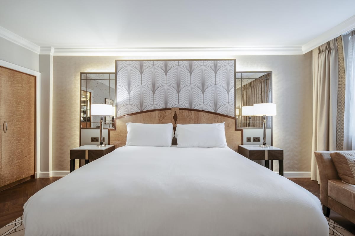 A large bed with white linens, two bedside tables with lamps, a wooden headboard, and a large mirror on the wall.