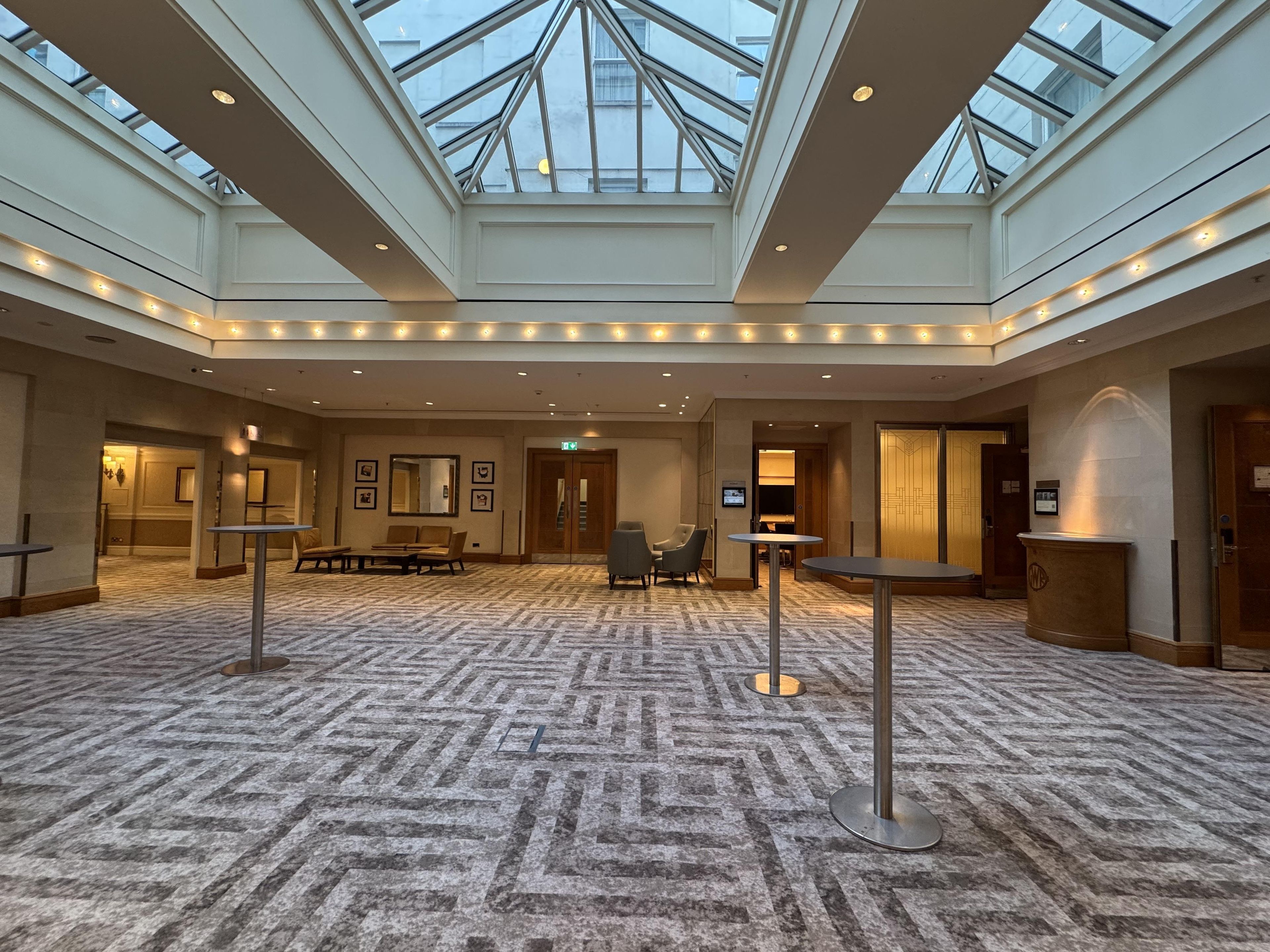 Un amplio vestíbulo de hotel con techo alto, tragaluces y alfombra estampada.