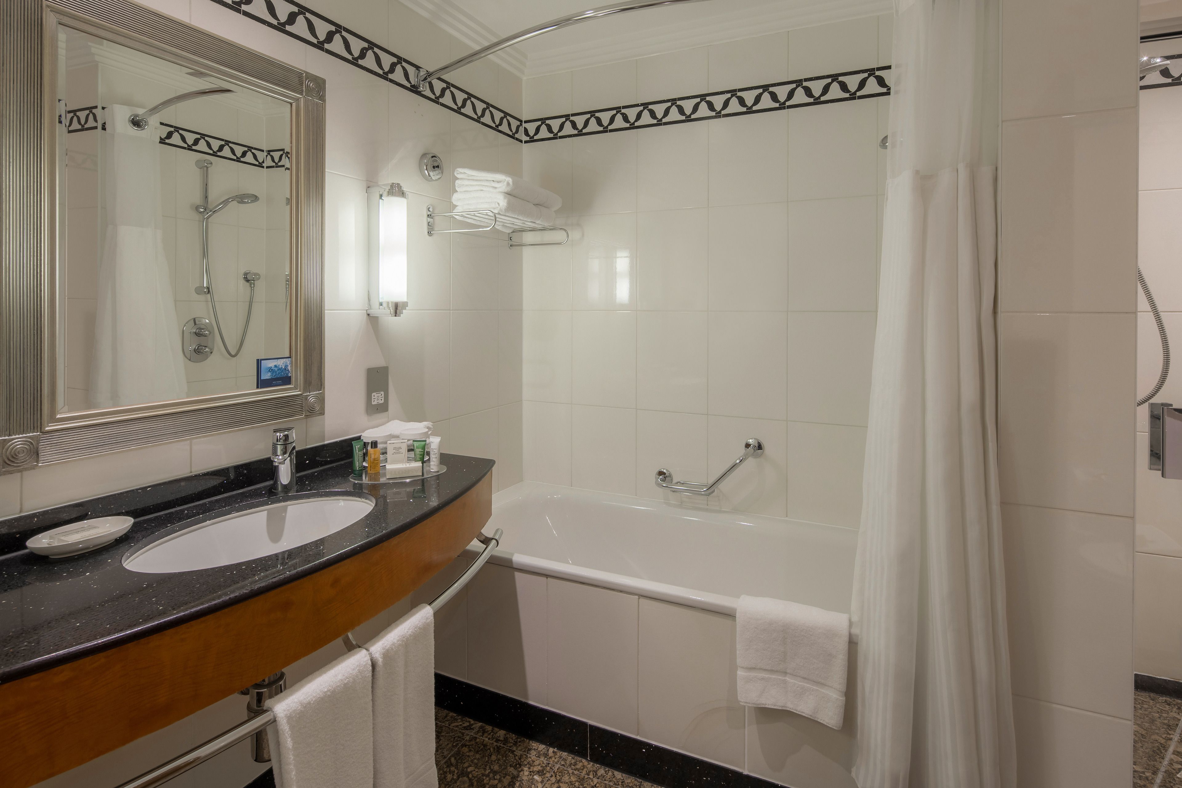 A bathroom with a white bathtub, a sink with a black countertop, and a shower area with a white curtain.